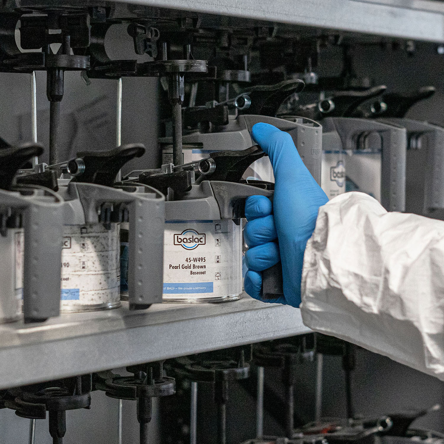 A hand in PPE picking some paint from a paint mixing rack.