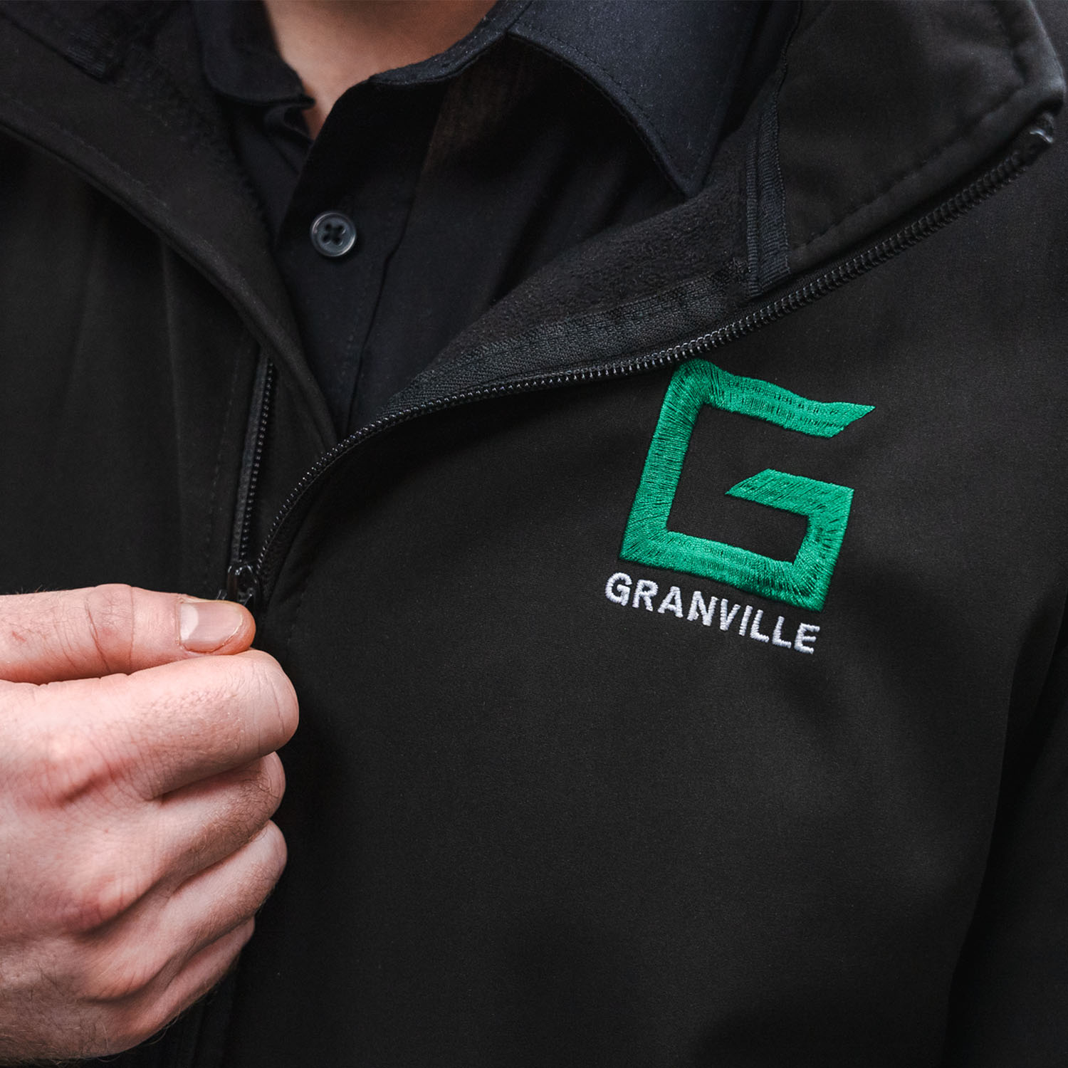 Closeup of a Granville Supplies employee zipping up their black business dress jacket and a Granville Supplies logo on the front.