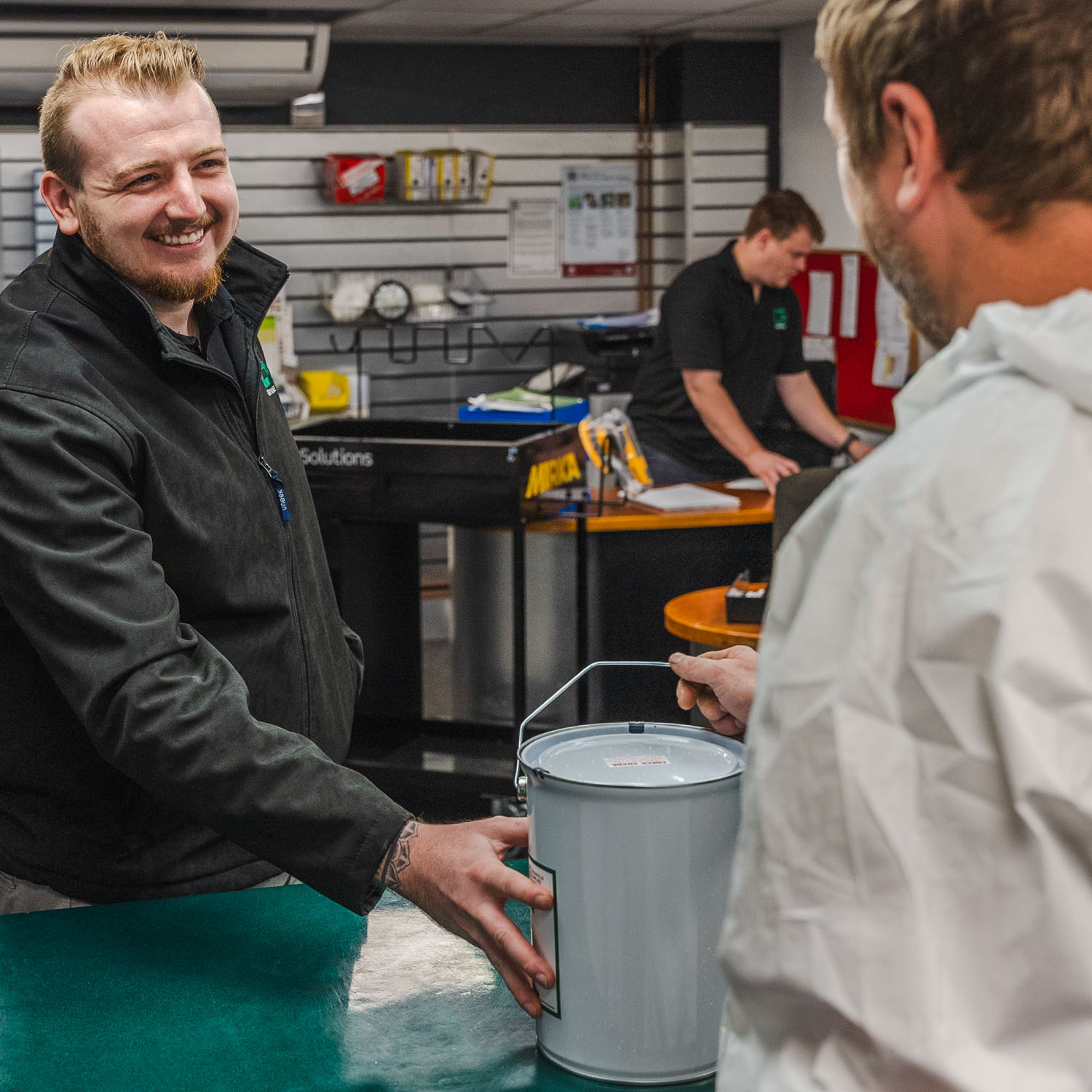 A Granville Supplies employee smiling at a customer as he hands over a tin of paint.