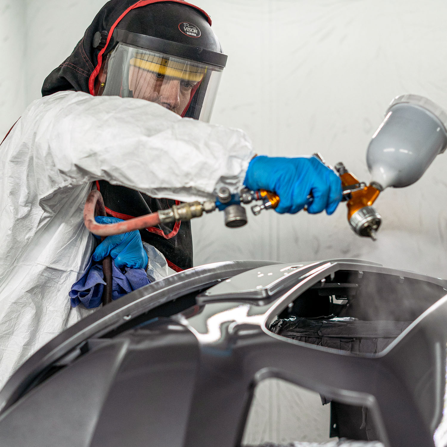 Automotive bodyshop technician in spray booth spraying a car body panel.