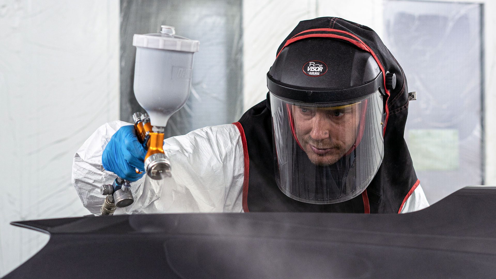Automotive bodyshop technician in spray booth spraying a car body panel.